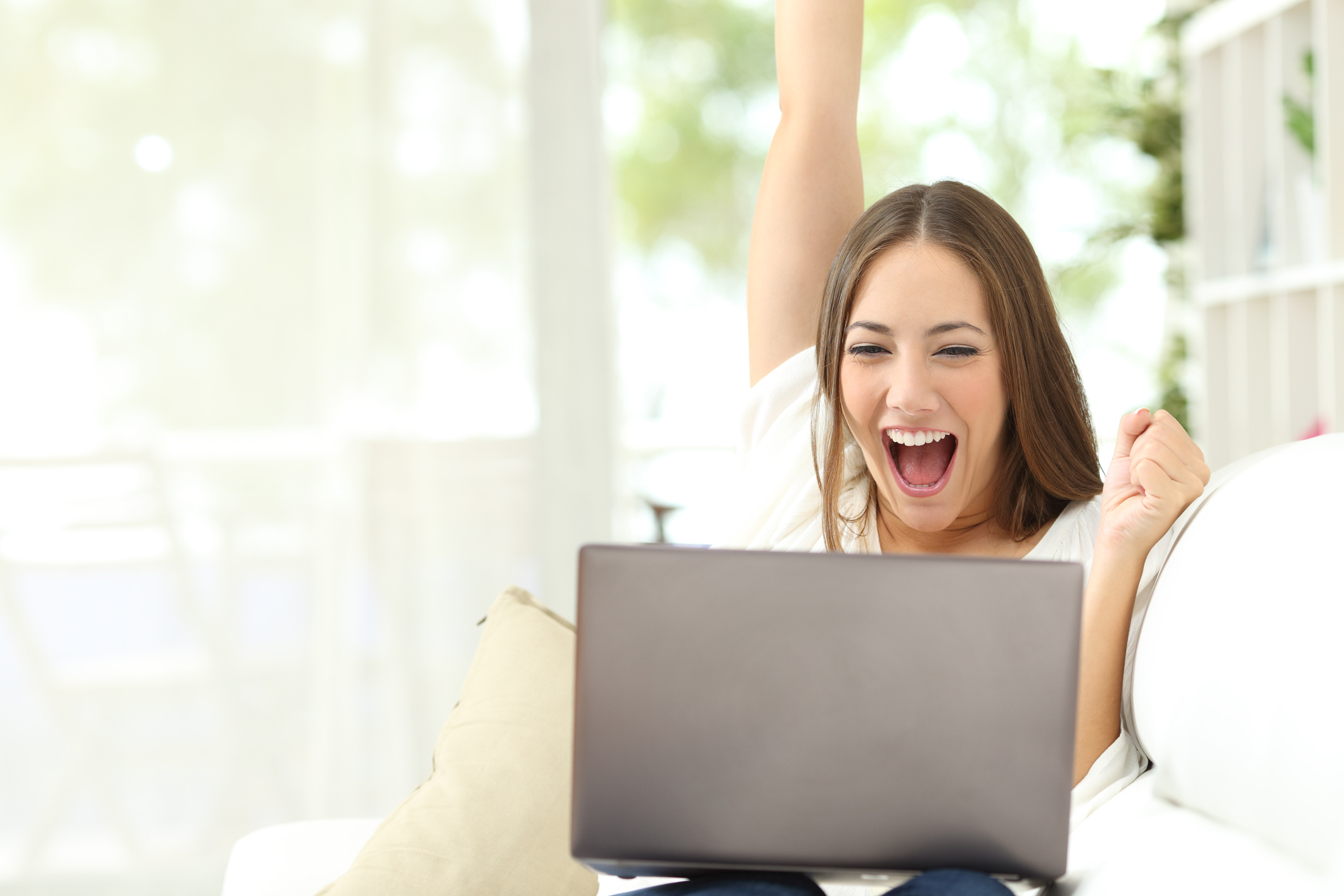 Excited girl celebrating good news on laptop sitting on a couch at home